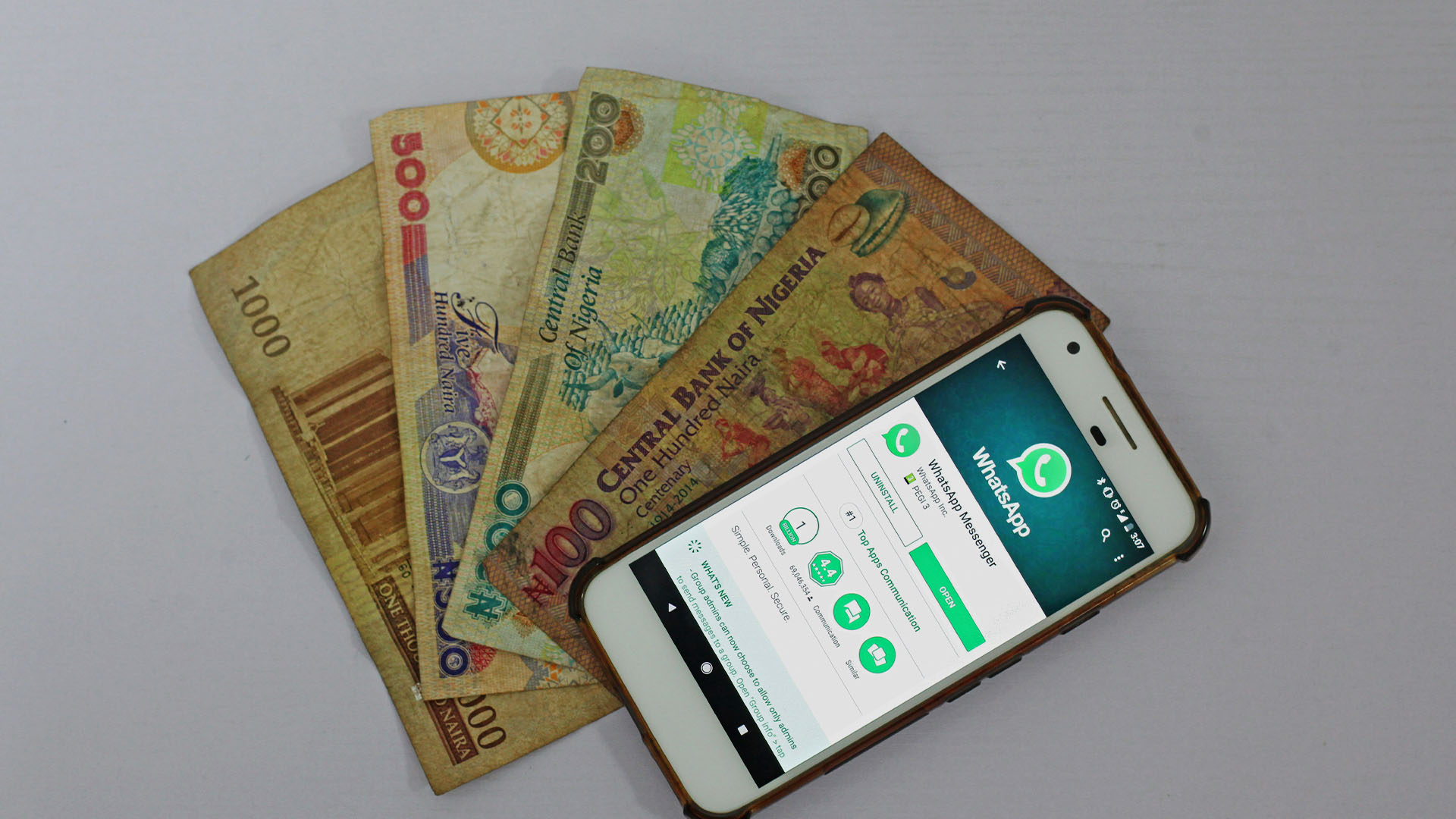 image of 3 nigerian currency note and a smartphone with whatsapp on playstore